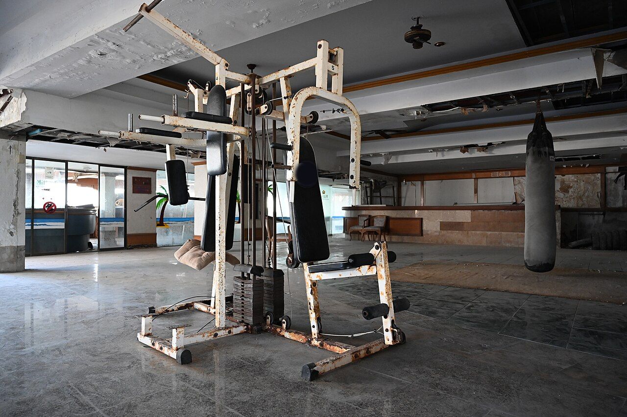 Une machine de musculation rouillée et un sac de frappe dans une salle de sport abandonnée