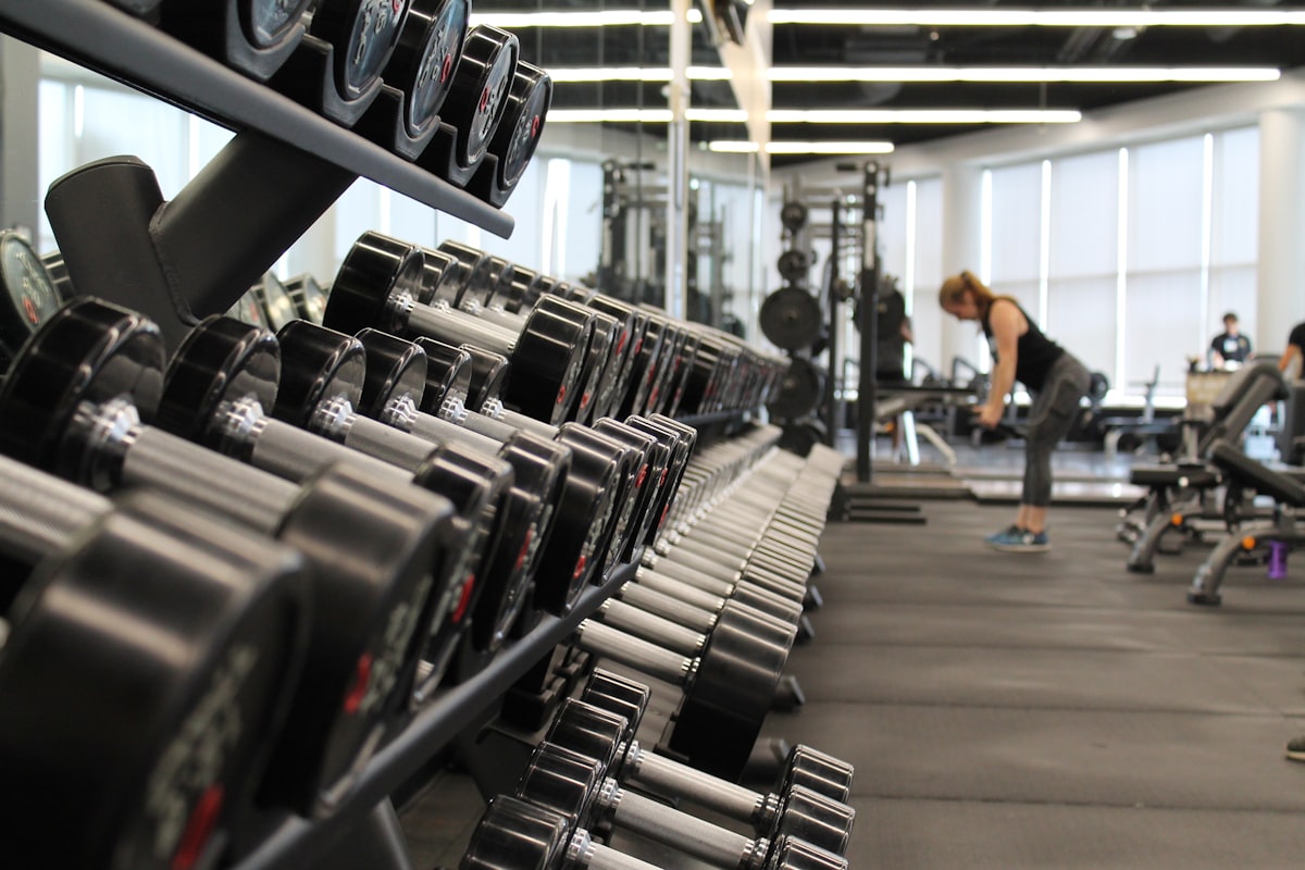 Salle de sport avec un rack d'haltères au premier plan et des machines au fond