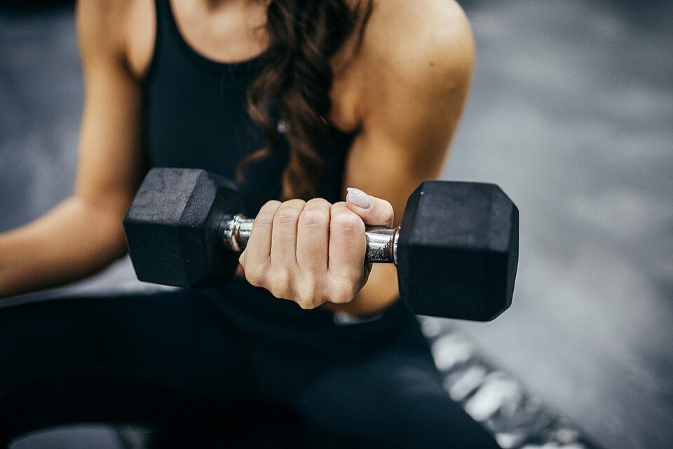 Gros plan sur une main qui serre un haltère noir pendant un curl biceps