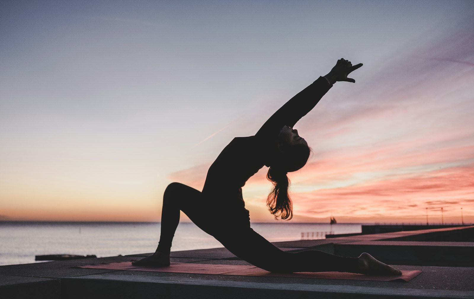 Silhouette d'une personne en fente basse, un bras tendu vers le ciel, devant un coucher de soleil