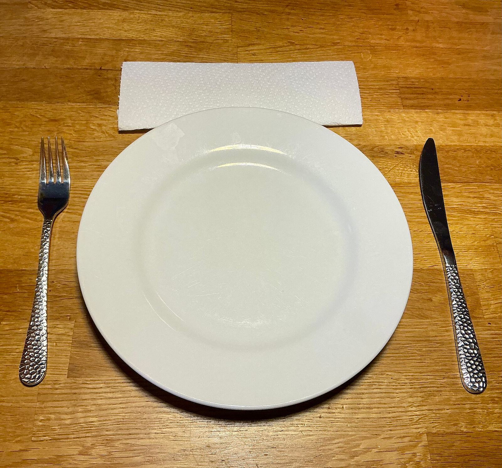Une assiette blanche vide entre une fourchette et un couteau, sur une table en bois