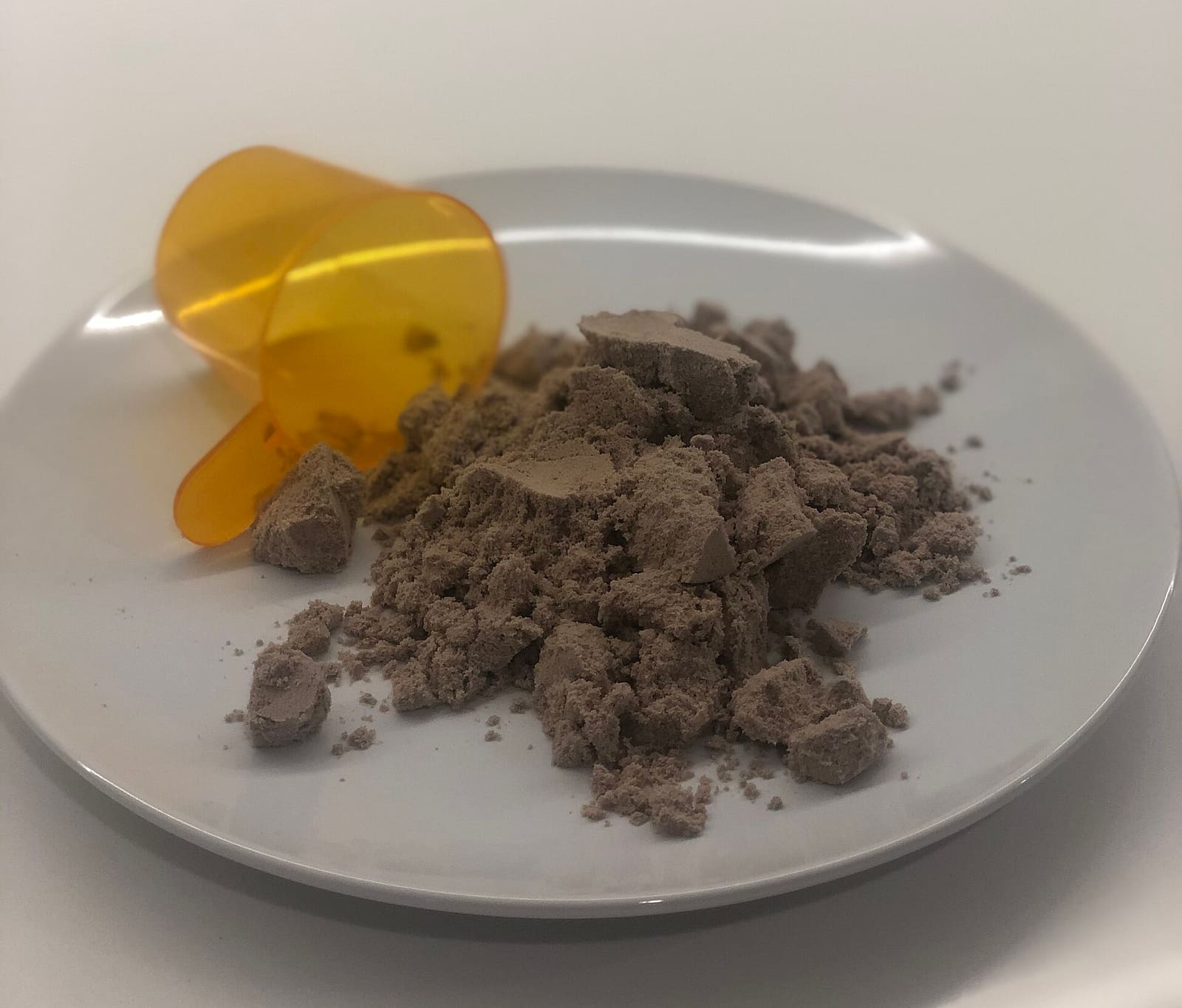 Une dosette en plastique orange renversée à côté d'un tas de poudre sur une assiette blanche