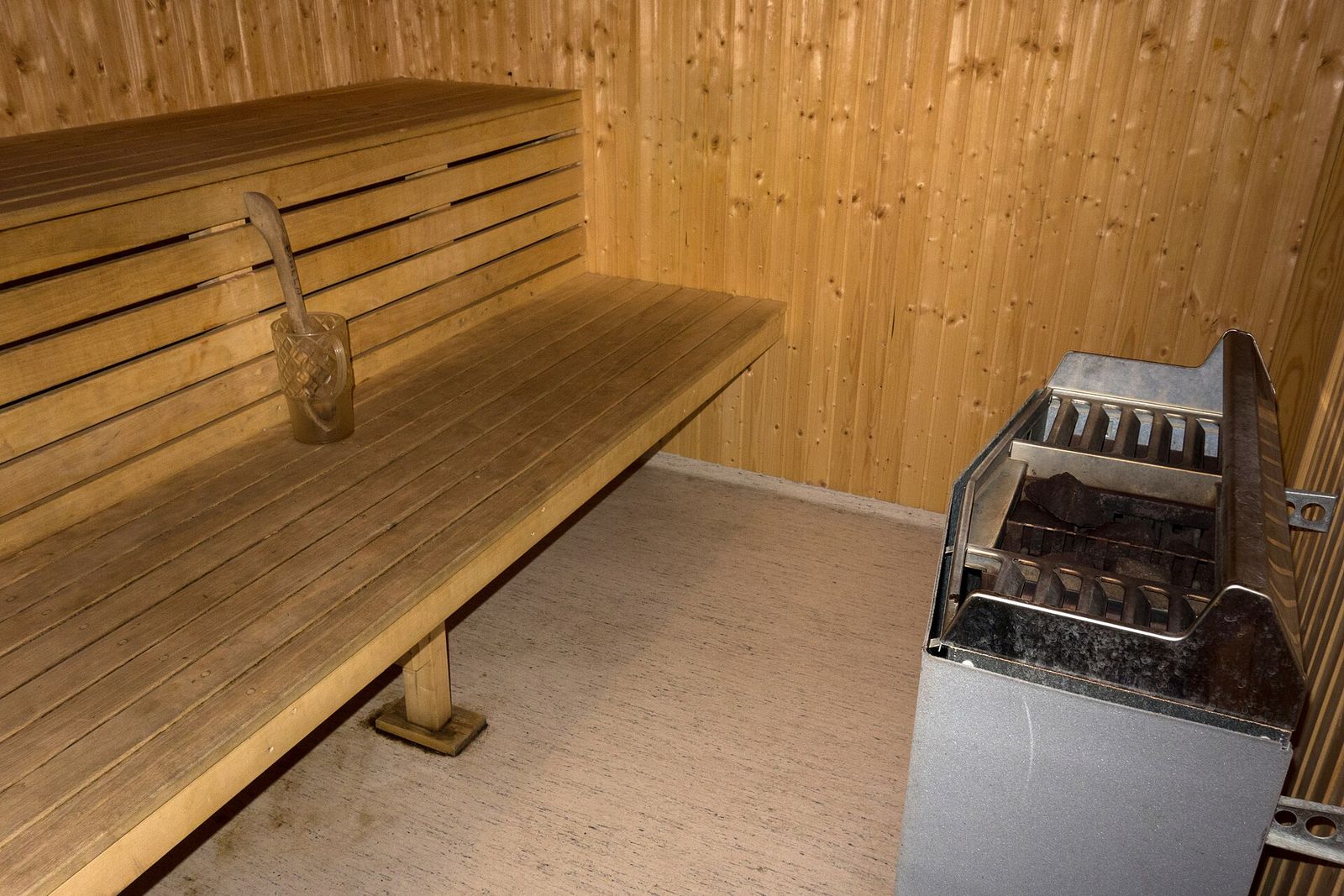 Intérieur d'un sauna vide, avec des banquettes en bois, un seau et sa louche, et un poêle à pierres