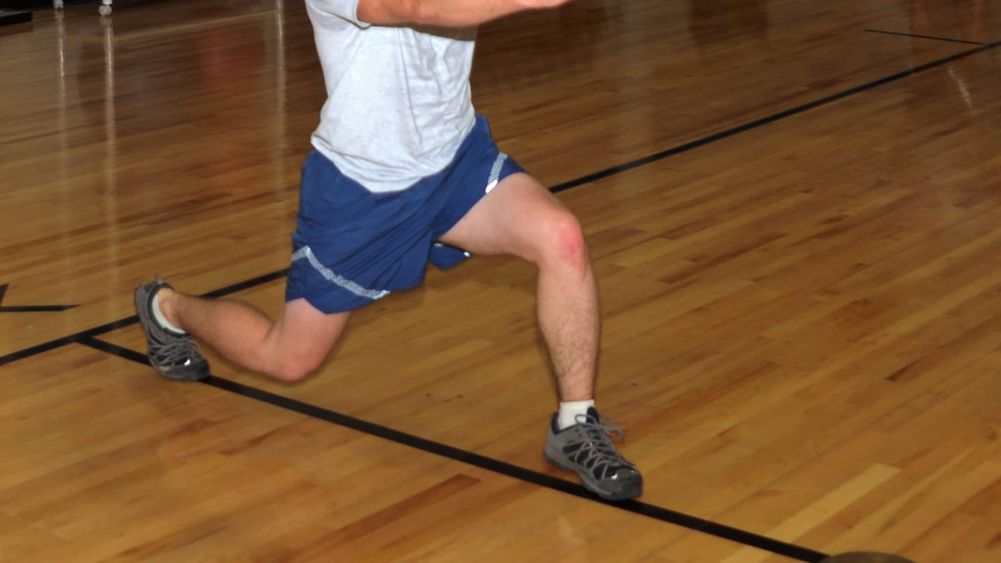 Jambes d'un homme en short bleu faisant une fente sur le parquet d'une salle de sport